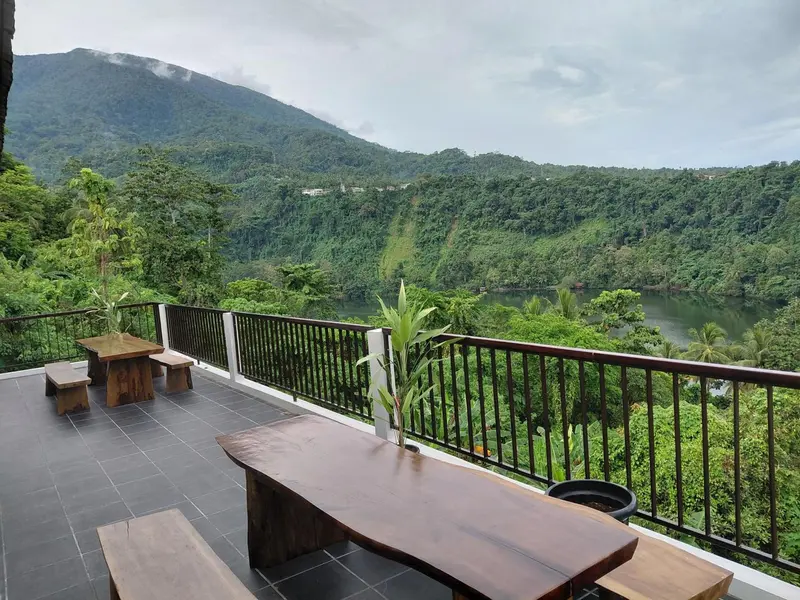 Terrasse avec mobilier en bois donnant sur une vallée verdoyante et un lac.