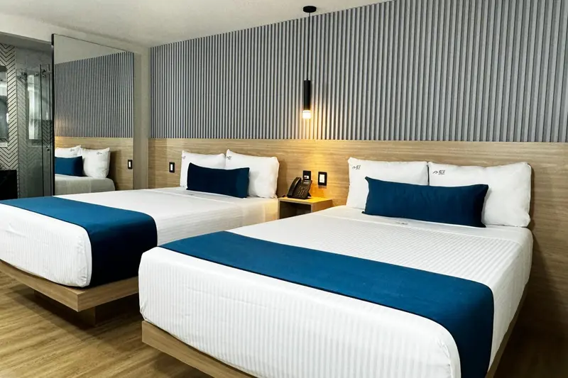Deux lits jumeaux avec une couverture bleue sont disposés dans une chambre d'hôtel moderne.