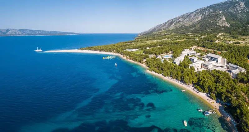 Vue aérienne d'une plage de sable fin bordée d'une eau turquoise et d'une végétation luxuriante.