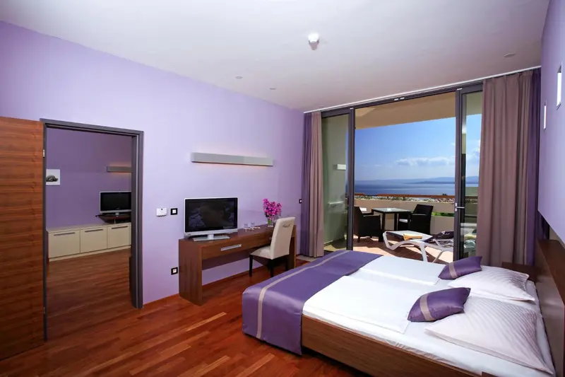 Chambre moderne avec un grand lit et une vue sur la mer depuis une terrasse.