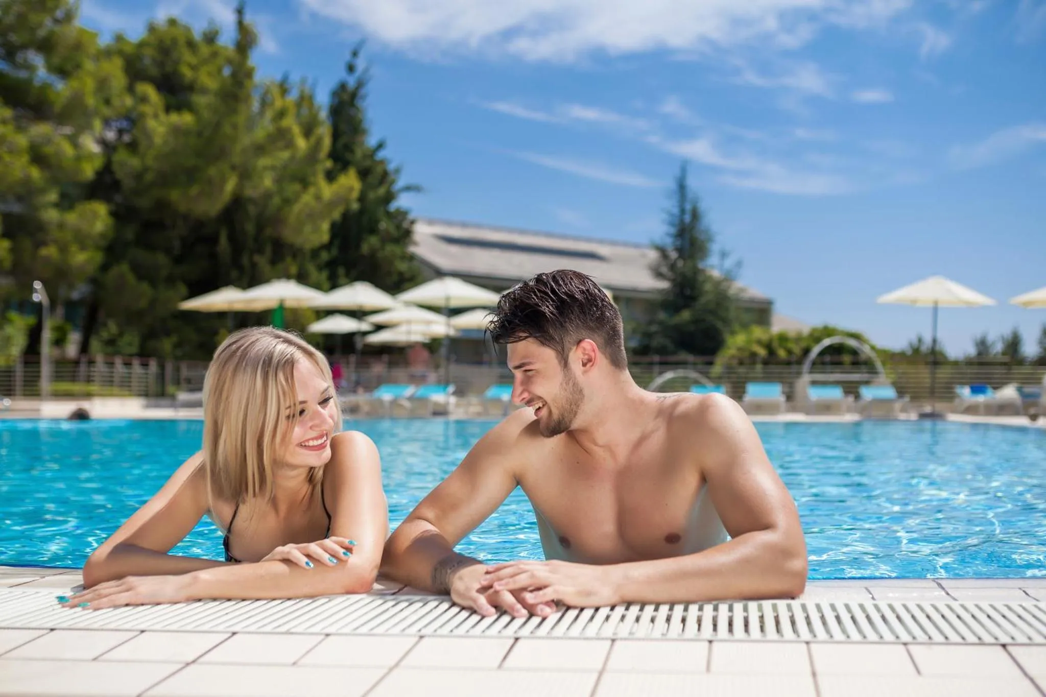 Un couple souriant se détend au bord d'une piscine ensoleillée.