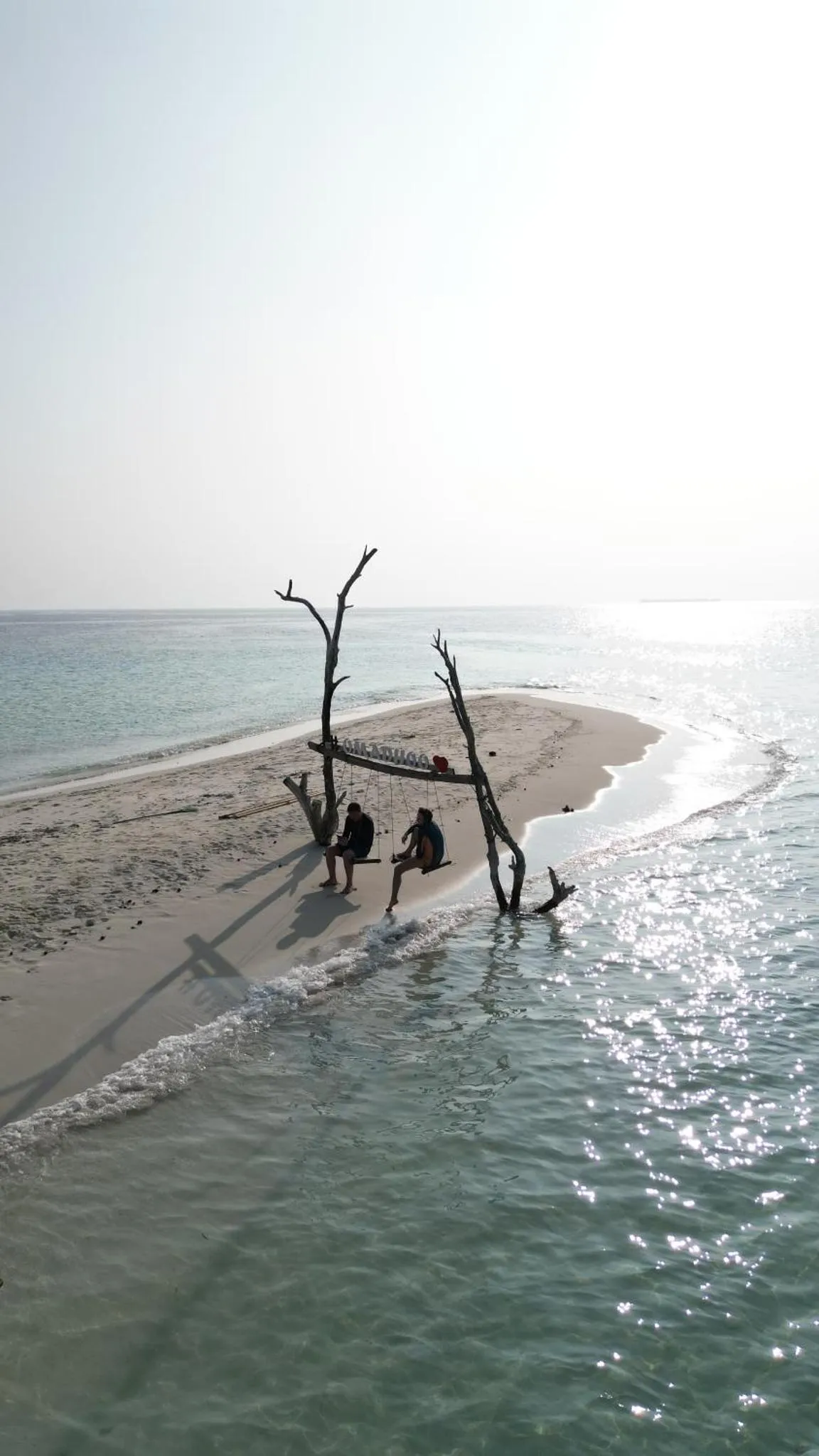 Trois personnes assises sur une structure en bois dans une eau turquoise peu profonde.
