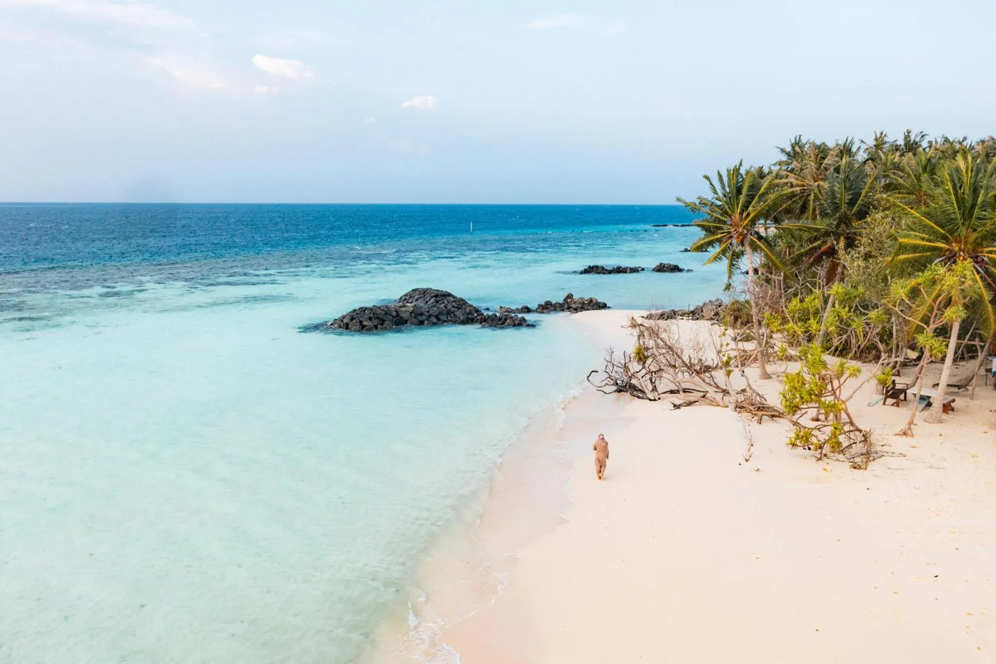 Plage de sable blanc bordée d'une eau turquoise et de végétation tropicale.