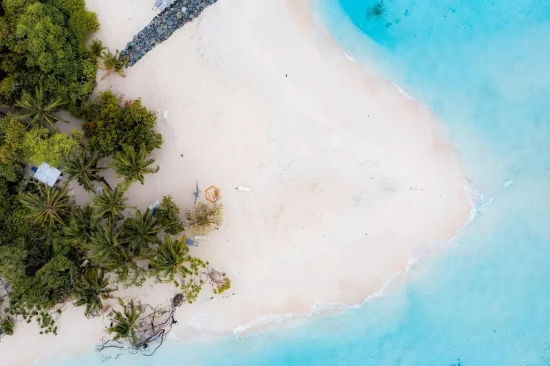 Vue aérienne d'une plage de sable blanc bordée de végétation luxuriante et d'eaux turquoise.
