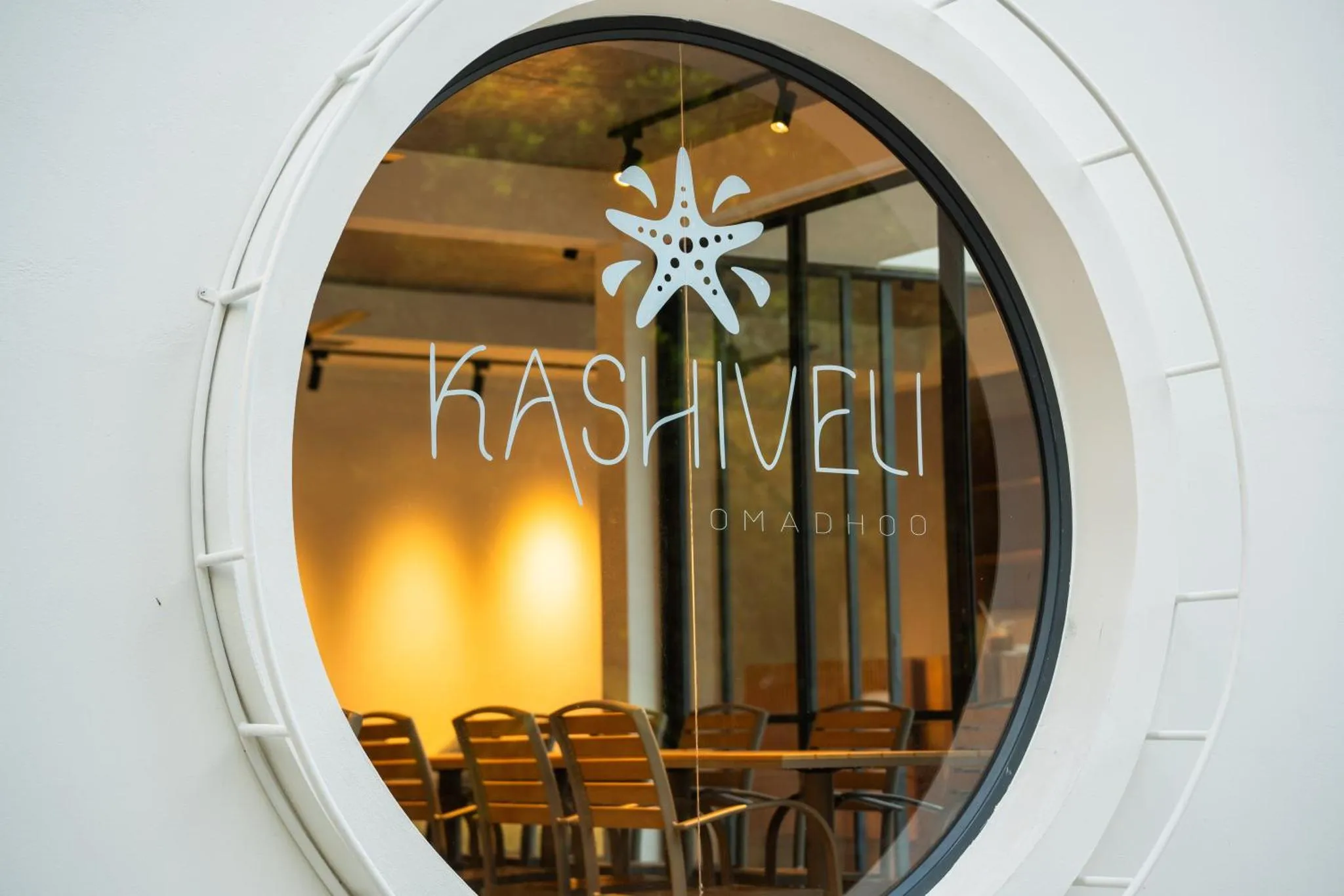 Une salle à manger lumineuse est visible à travers une fenêtre circulaire.