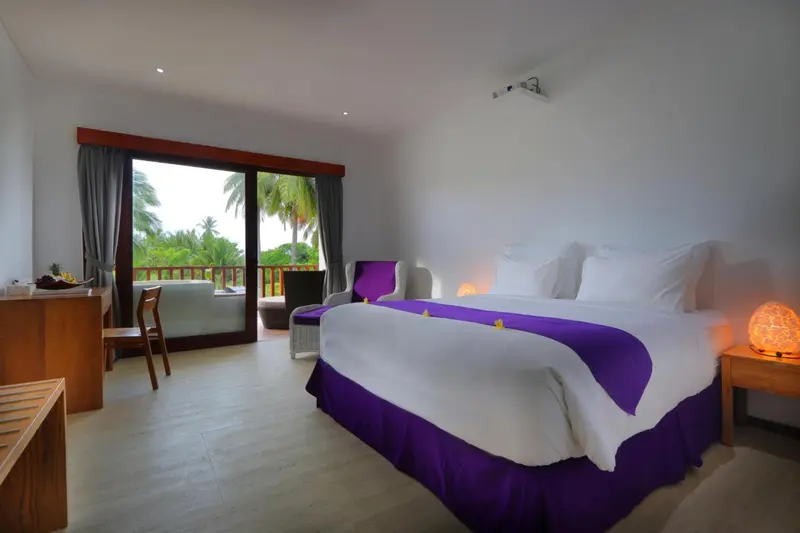 Chambre lumineuse avec un grand lit et vue sur la végétation.