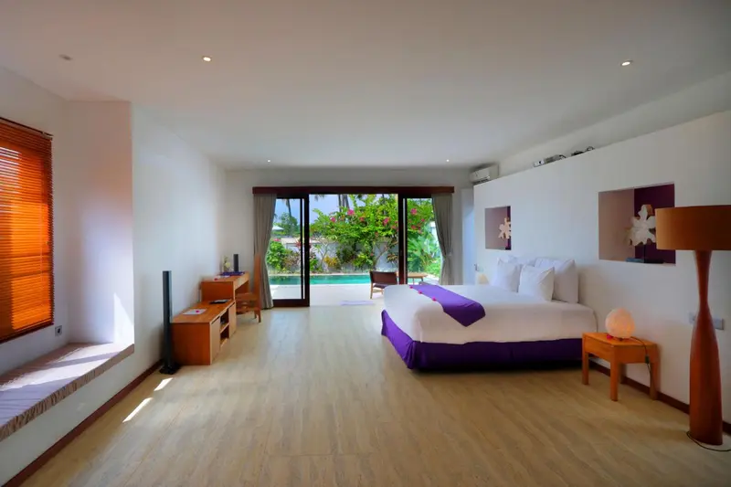 Une chambre lumineuse avec un grand lit et un accès à une piscine.