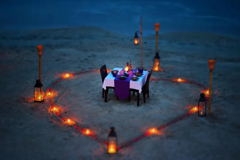 Table dressée pour un dîner romantique sur une plage éclairée aux chandelles.