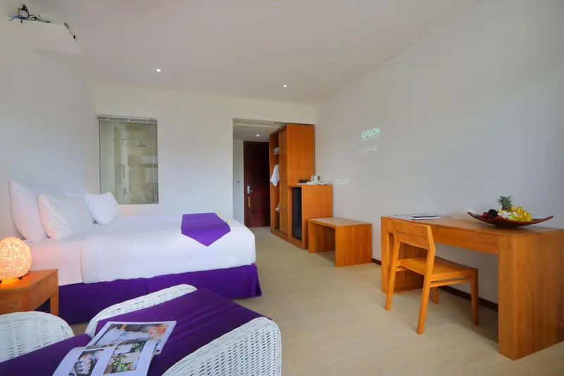 Une chambre lumineuse avec un lit recouvert d'une courtepointe violette et d'oreillers blancs.