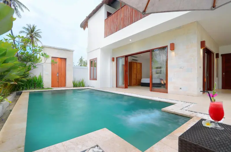 Une piscine turquoise invite à la détente devant une villa au toit de chaume.