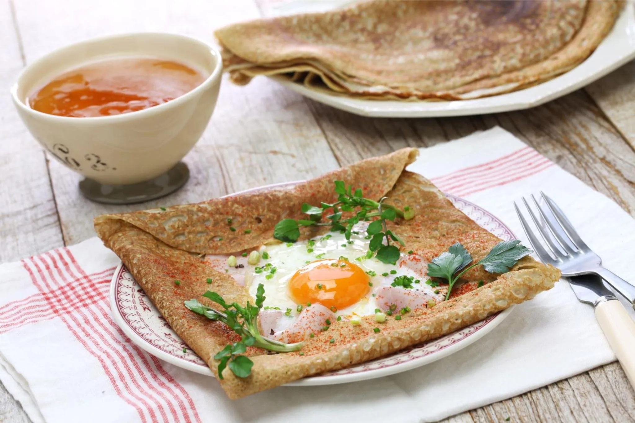 Assiette de galette bretonne garnie d'un œuf au plat et d'une sauce.