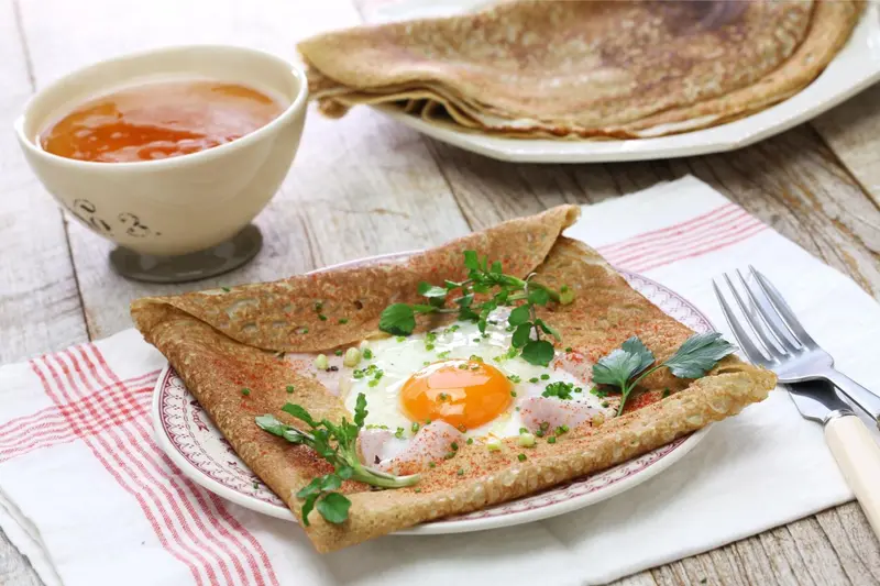 Assiette de galette bretonne garnie d'un œuf au plat et d'une sauce.
