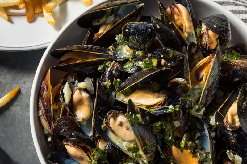 Un plat de moules et de frites est présenté dans un bol blanc.
