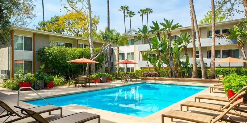 Une piscine turquoise entourée de chaises longues et de végétation luxuriante devant un bâtiment à deux étages.