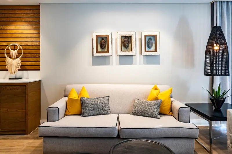 Un canapé gris avec des coussins jaunes et à motifs est placé devant un mur décoré.