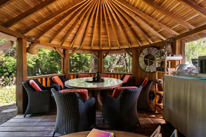 Une table ronde et des chaises sont disposées sous une structure en bois ouverte.