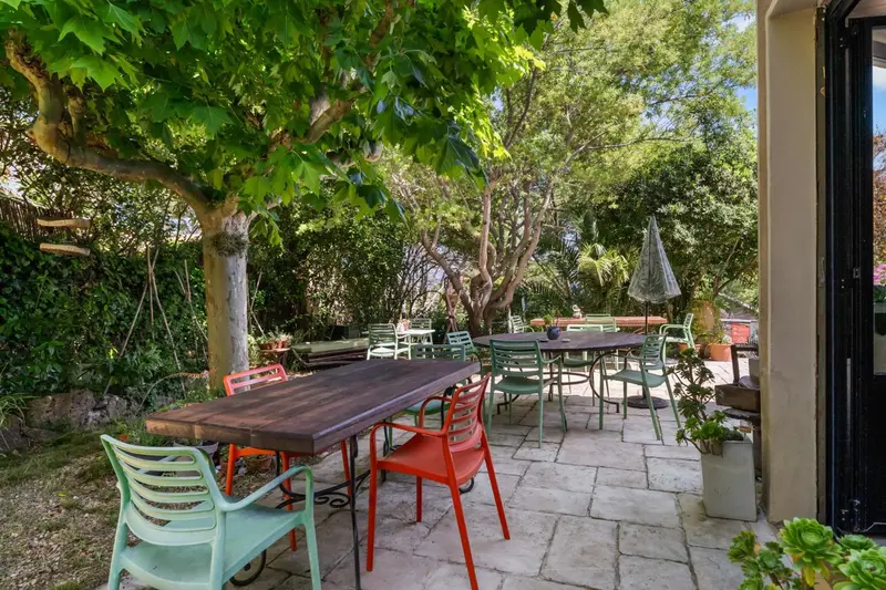 Terrasse pavée avec tables et chaises colorées sous des arbres.