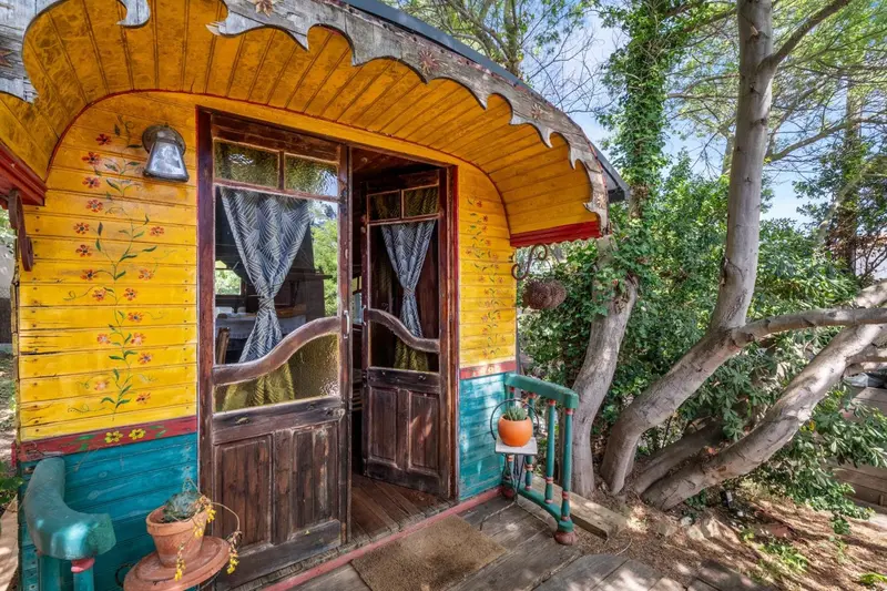 Petite cabane colorée avec une porte ouverte et des fleurs peintes.