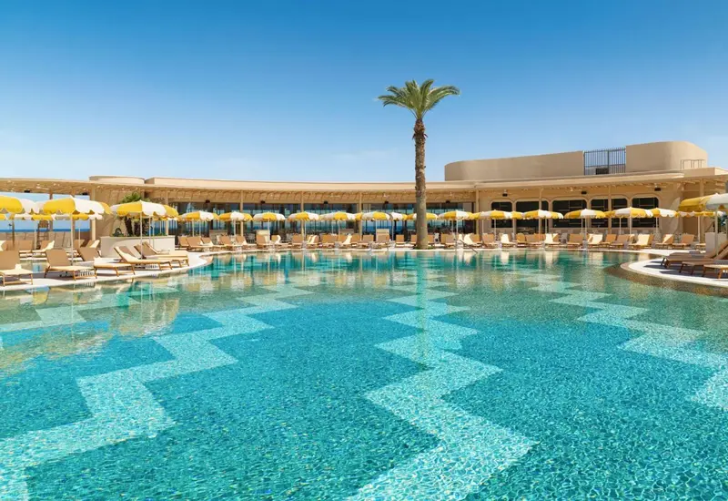 Une piscine rectangulaire turquoise avec un motif géométrique au fond, entourée de transats et de parasols.