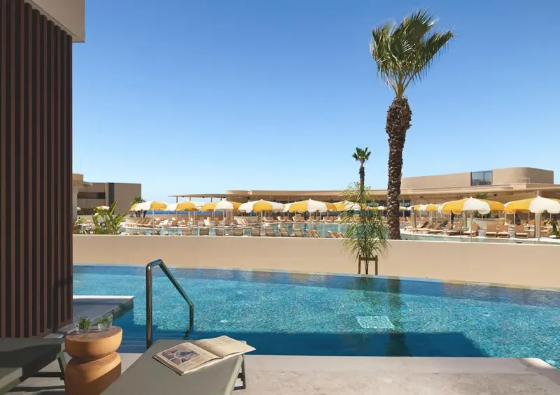 Une piscine à débordement offre une vue sur un ensemble de transats et de parasols.