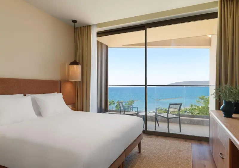 Chambre lumineuse avec un grand lit donnant sur une vue mer et une terrasse.