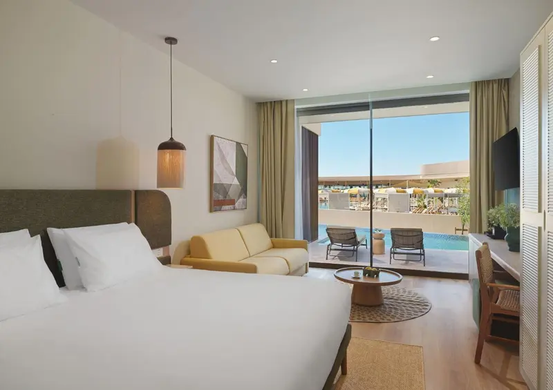 Une chambre lumineuse avec un canape et un accès à une terrasse avec piscine.