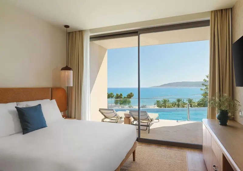 Une chambre lumineuse avec un grand balcon donnant sur la mer.