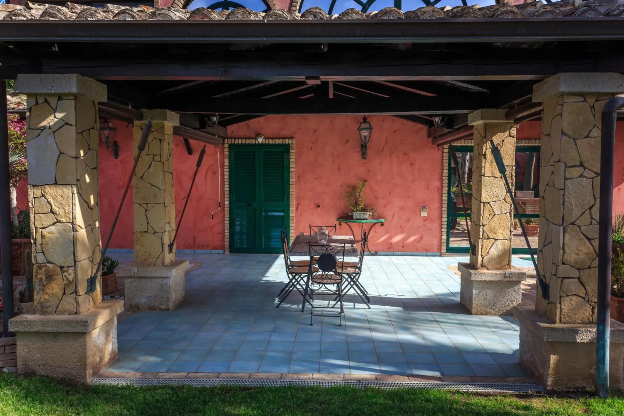 Terrasse ombragée avec table et chaises en fer forgé.