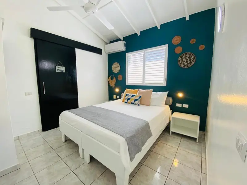 Une chambre lumineuse avec un grand lit recouvert d'une courtepointe grise et de coussins colorés.
