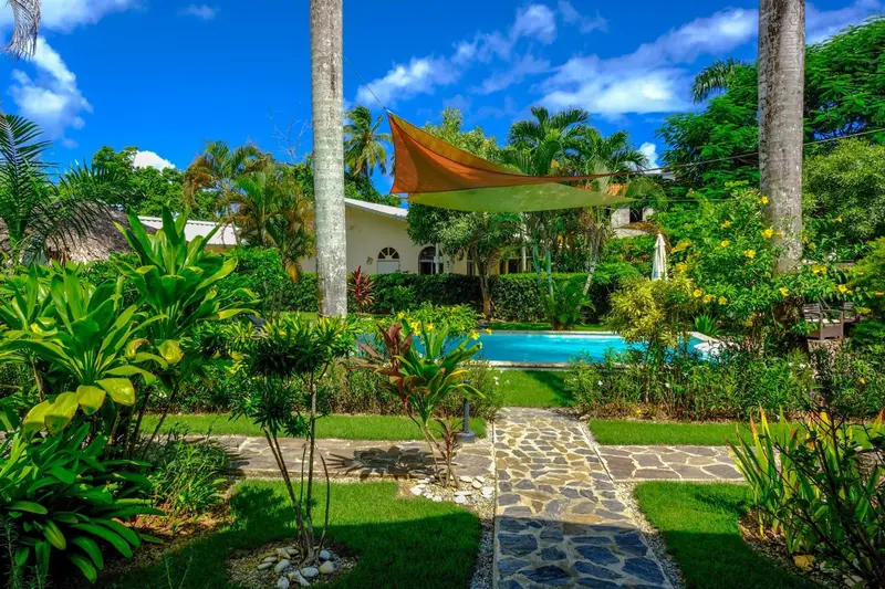 Jardin luxuriant avec piscine et allée pavée menant à une habitation.