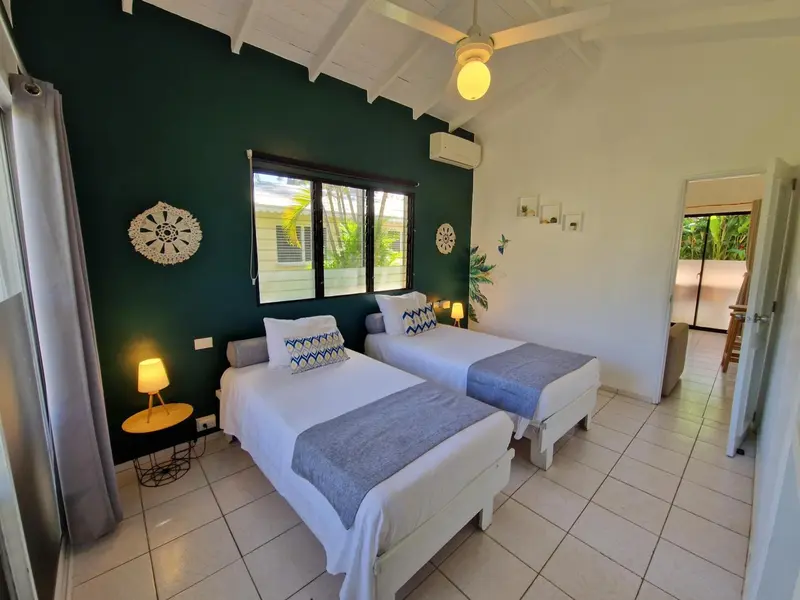 Chambre lumineuse avec deux lits simples et décoration murale.