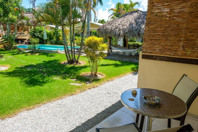 Une terrasse avec une table et des chaises donne sur une piscine et un jardin tropical.