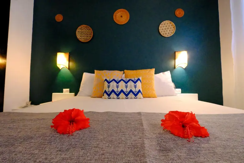 Un lit recouvert d'une courtepointe grise et de coussins colorés se trouve devant un mur bleu décoré.