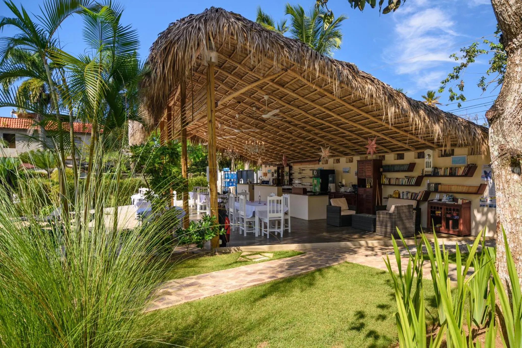 Un espace ombragé abrite des tables et un comptoir de boissons dans un jardin tropical.