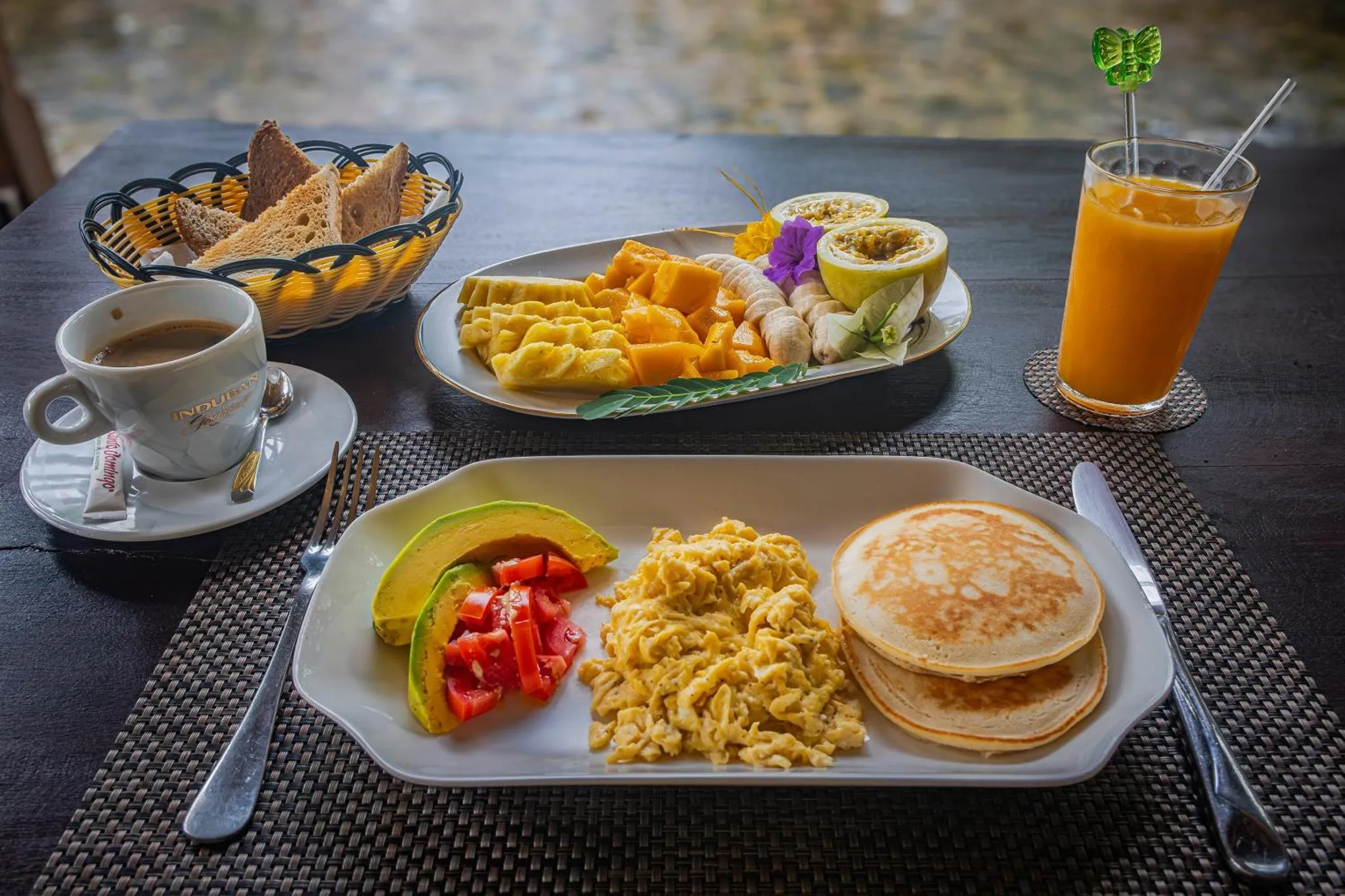 Une table est dressée avec un petit-déjeuner composé de fruits frais, de crêpes et d'œufs brouillés.