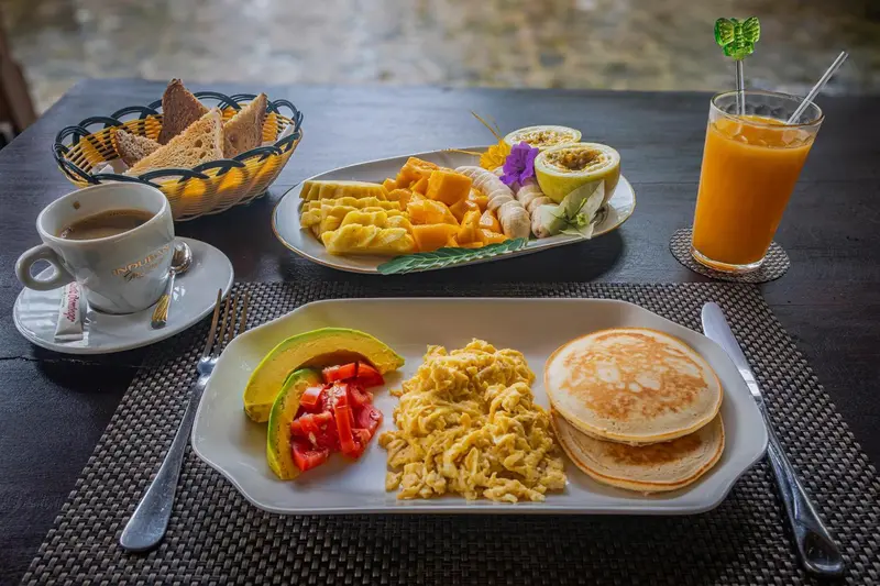 Une table est dressée avec un petit-déjeuner composé de fruits frais, de crêpes et d'œufs brouillés.