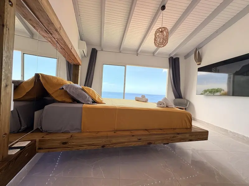 Une chambre lumineuse avec un grand lit donnant sur une vue mer.