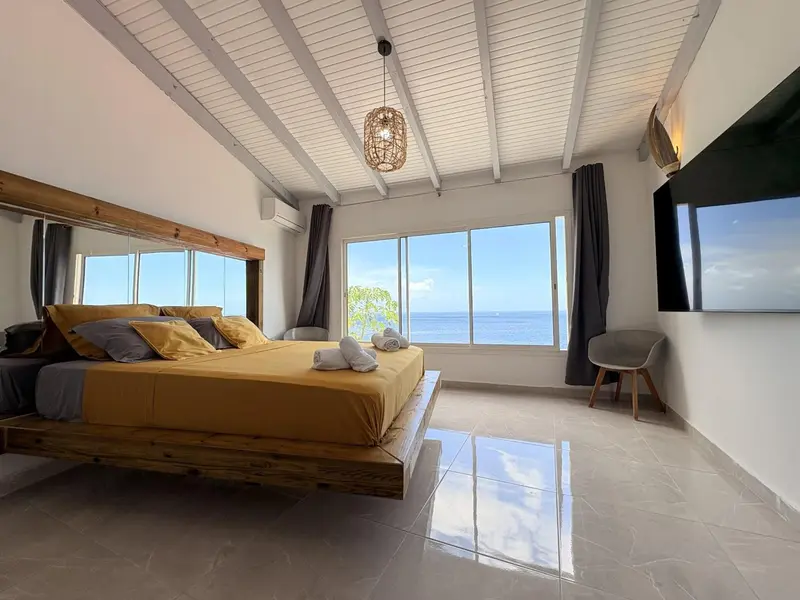 Une chambre lumineuse avec un grand lit face à une baie vitrée donnant sur la mer.
