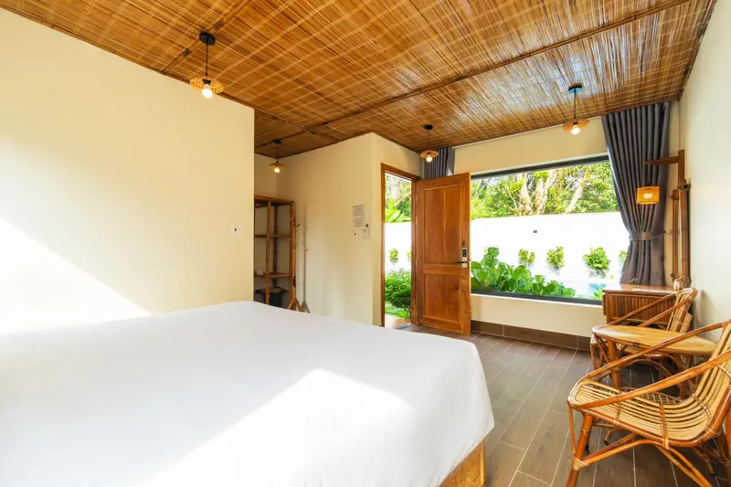 Une chambre lumineuse avec un lit blanc et une porte ouverte sur une végétation luxuriante.