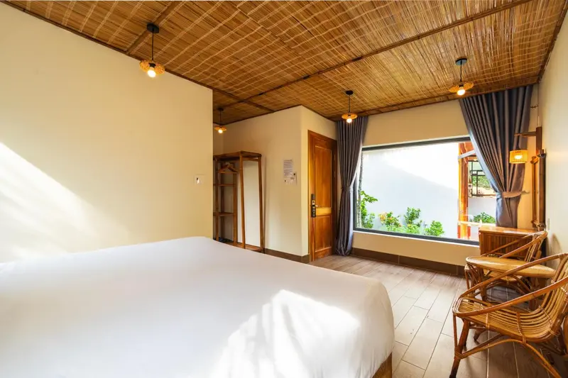Une chambre lumineuse avec un lit blanc et une fenêtre donnant sur la végétation.