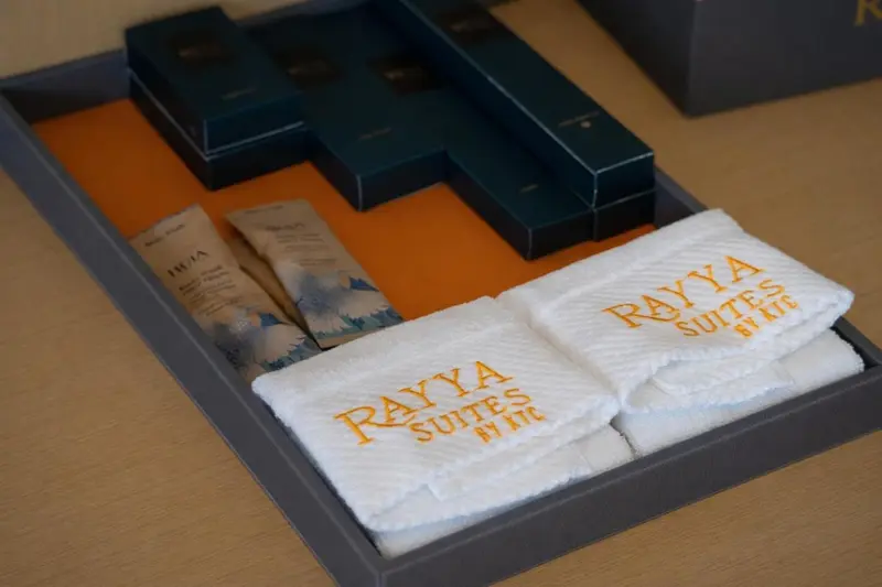 Des articles de toilette disposés sur un plateau orange et des serviettes brodées sur un lit.
