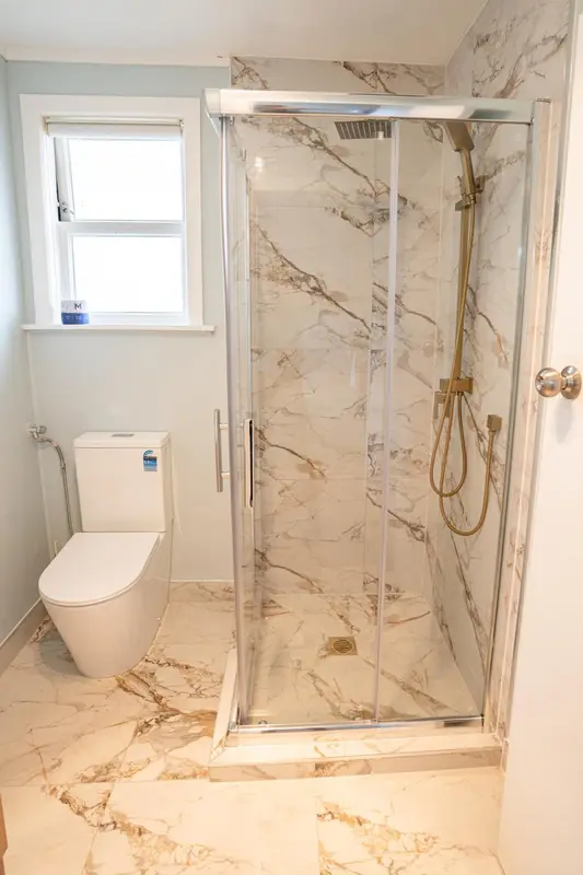 Une douche à l'italienne moderne avec des carreaux de marbre et une pomme de douche dorée.