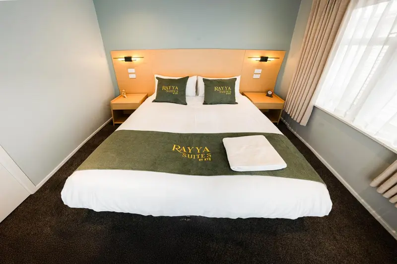 Un lit double avec une couverture verte et des oreillers dans une chambre d'hôtel.