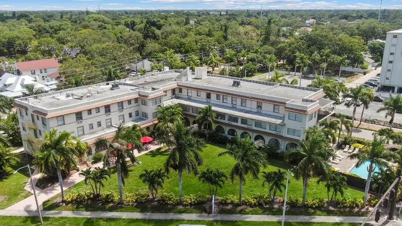 Vue aérienne d'un bâtiment blanc entouré de végétation luxuriante et d'une pelouse verdoyante.