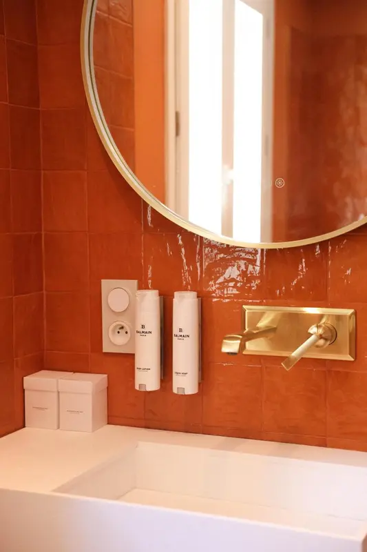 Un miroir rond au-dessus d'un lavabo dans une salle de bain carrelée.