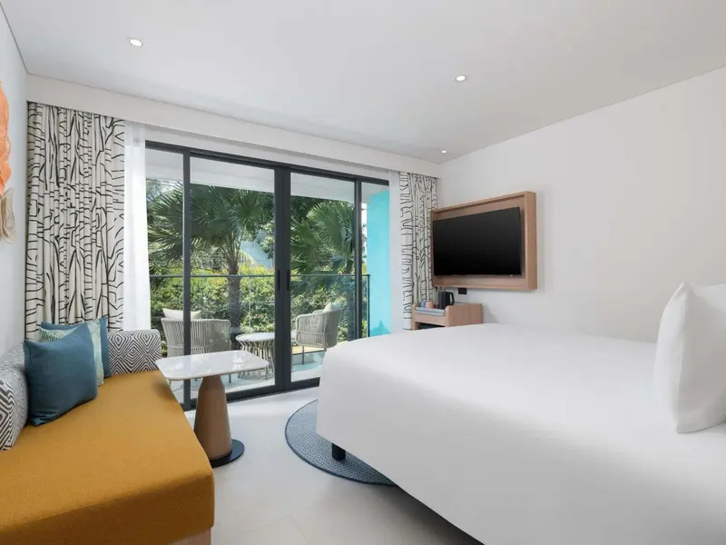 Une chambre lumineuse avec un grand lit et un espace salon donnant sur une terrasse.