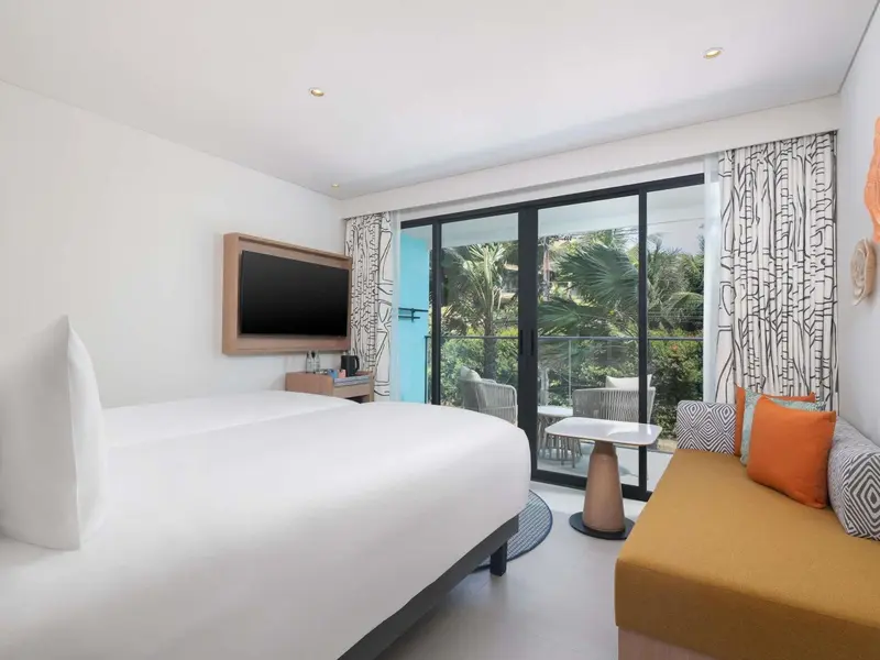 Une chambre lumineuse avec un grand lit et un coin salon donnant sur une terrasse.