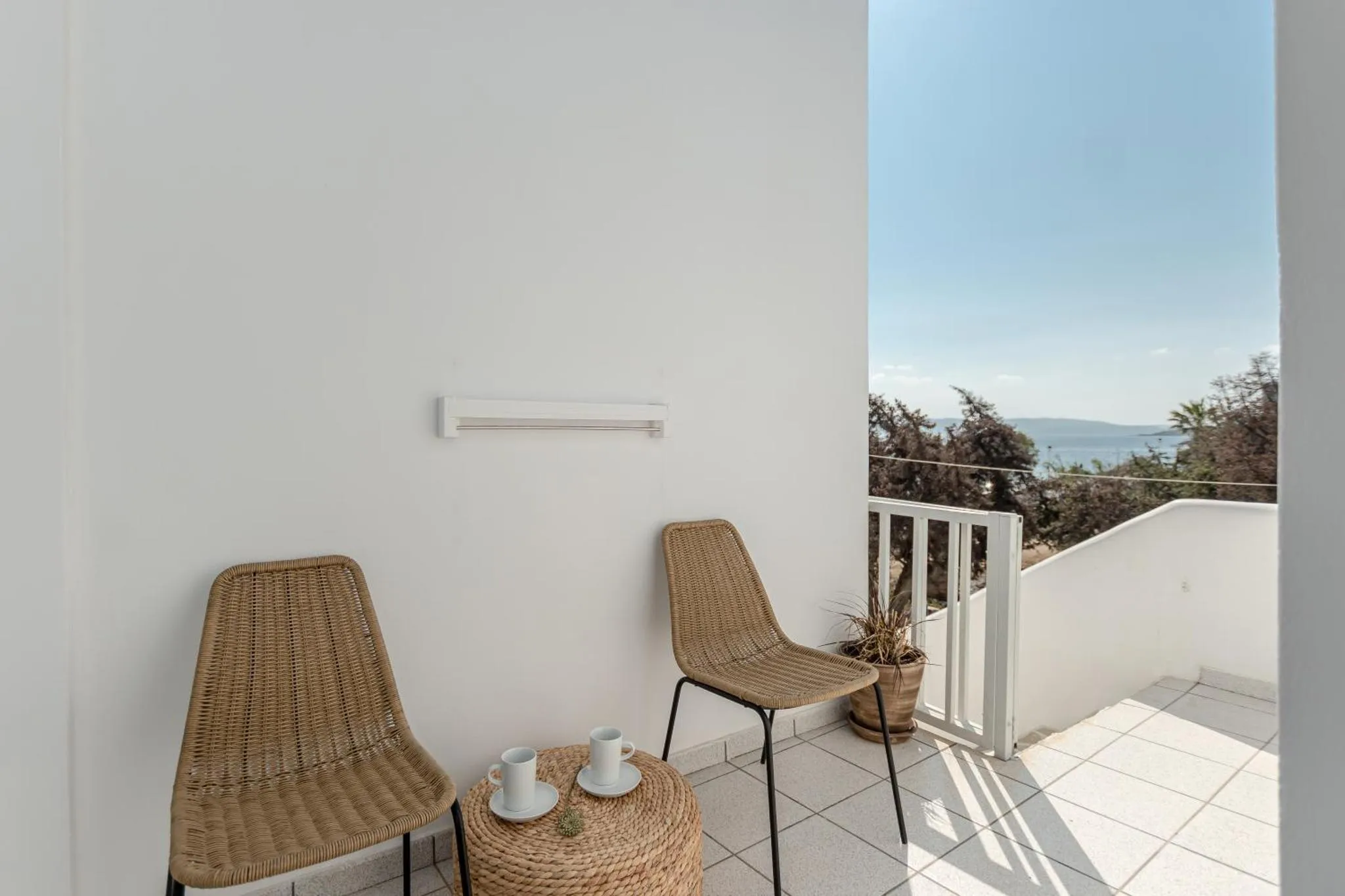 Deux fauteuils en rotin et une petite table sur une terrasse ensoleillée avec vue sur la mer.
