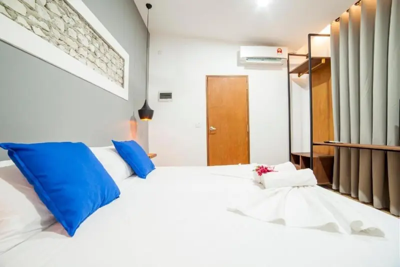 Une chambre lumineuse avec un grand lit recouvert de draps blancs et de coussins bleus.