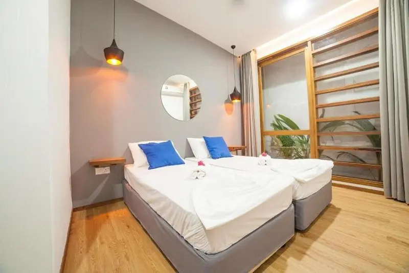 Deux lits simples dans une chambre lumineuse avec des oreillers bleus et une décoration sobre.